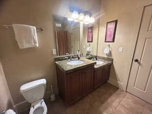 Bathroom with toilet, tile patterned floors, and dual bowl vanity