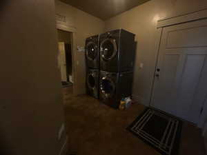 Laundry area featuring dark tile patterned floors and stacked washing maching and dryer