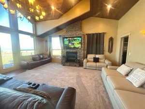 Living room with carpet, a stone fireplace, high vaulted ceiling, and wood ceiling