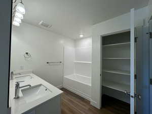 Bathroom featuring a dual vanity, wood-type flooring, linen storage, and  shower combination