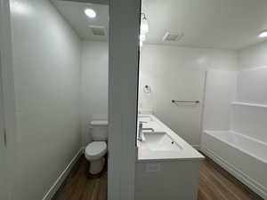 Full bathroom featuring toilet room, double sink vanity, bathtub / shower combination, and hardwood / wood-style floors