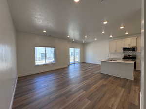 Living room open into Dining area and Kitchen with white cabinets, stainless steel appliances, an island with sink, and LVP flooring