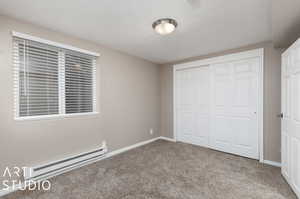 Unfurnished bedroom featuring a closet, baseboard heating, and carpet flooring