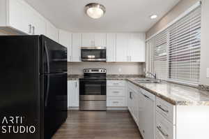 Kitchen with white cabinetry, dark hardwood / wood-style flooring, light stone countertops, appliances with stainless steel finishes, and sink