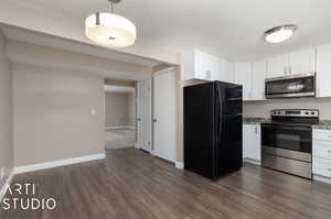 Kitchen with stainless steel appliances, light stone counters, hanging light fixtures, white cabinetry, and dark wood-type flooring