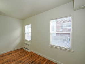 Empty room with dark wood-type flooring and a wall unit AC