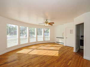 Unfurnished living room with radiator, ceiling fan, hardwood / wood-style flooring, and a wealth of natural light