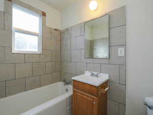 Full bathroom with vanity, tiled shower / bath combo, toilet, and tile walls