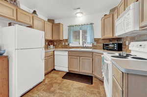 Kitchen with decorative backsplash, light tile patterned floors, white appliances, and sink