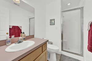 Bathroom featuring vanity, a shower with door, tile patterned flooring, and toilet