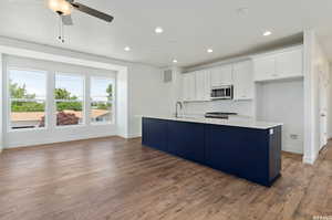 Kitchen featuring ceiling fan, light wood-type flooring, tasteful backsplash, and a center island with sink