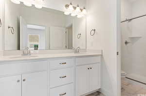 Bathroom featuring dual vanity, tiled shower, tile patterned floors, and toilet