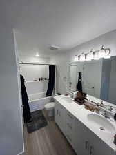 Full bathroom featuring dual vanity, a textured ceiling, hardwood / wood-style flooring, and shower / bath combination with curtain