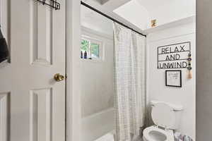 Bathroom featuring shower / bathtub combination with curtain and toilet