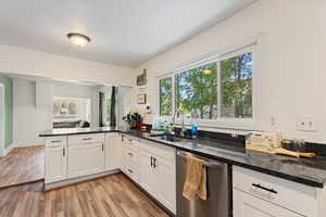 Kitchen with light wood-type flooring, dishwasher, kitchen peninsula, and dark stone counters