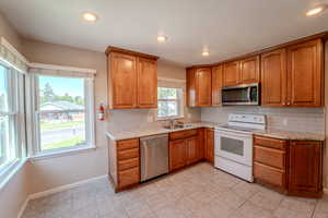 Kitchen with appliances with stainless steel finishes, sink, light stone counters, backsplash, and light tile patterned flooring