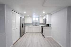 Kitchen featuring white cabinetry, new light hardwood / wood-style floors, appliances with stainless steel finishes, decorative backsplash, and sink