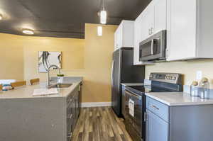 Kitchen featuring stainless steel appliances, sink, light stone counters, pendant lighting, and dark hardwood / wood-style floors