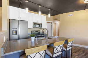 Kitchen with white cabinets, dark wood-type flooring, appliances with stainless steel finishes, and sink