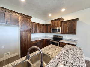 Kitchen featuring appliances with stainless steel finishes, dark brown cabinets, a textured ceiling, light stone countertops, and wood-type flooring