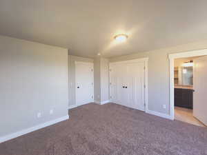 Unfurnished bedroom with a closet, connected bathroom, and light colored carpet