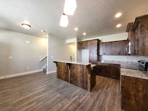 Kitchen with range with electric stovetop, light stone counters, dark brown cabinetry, a kitchen island, and dark hardwood / wood-style floors