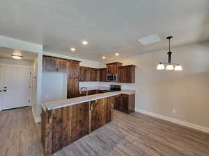 Kitchen with light hardwood / wood-style flooring, a kitchen island, light stone countertops, appliances with stainless steel finishes, and dark brown cabinetry