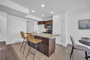 Kitchen featuring electric range, a breakfast bar area, an island with sink, light hardwood / wood-style floors, and dark brown cabinetry