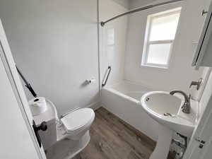 Bathroom with washtub / shower combination, hardwood / wood-style flooring, toilet, and plenty of natural light