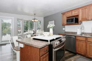 Kitchen with a chandelier, backsplash, dark wood-type flooring, a kitchen island, and appliances with stainless steel finishes