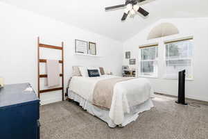 Carpeted bedroom with ceiling fan and vaulted ceiling