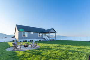 Back of property featuring a yard, a water view, and an outdoor fire pit