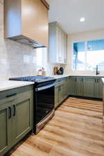 Kitchen featuring green cabinetry, backsplash, gas range, light wood-type flooring, and custom exhaust hood