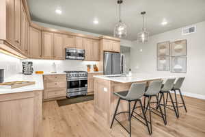 Kitchen featuring premium appliances, light brown cabinetry, light wood-type flooring, and an island with sink