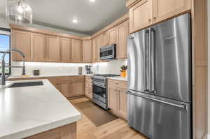 Kitchen with pendant lighting, light brown cabinets, sink, light hardwood / wood-style floors, and high quality appliances