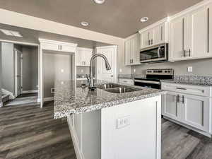 Kitchen featuring white cabinetry, stainless steel appliances, a kitchen island with sink, sink, and dark wood-type flooring