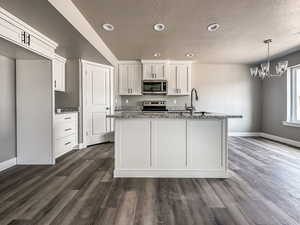 Kitchen with stone counters, stainless steel appliances, white cabinets, a kitchen island with sink, and dark wood-type flooring