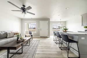 Living room with a textured ceiling, ceiling fan with notable chandelier, and light wood-type flooring