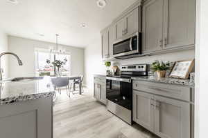 Kitchen with appliances with stainless steel finishes, light stone counters, gray cabinets, and light hardwood / wood-style floors