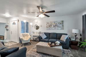 Living room with a textured ceiling, carpet, and ceiling fan