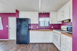 Kitchen featuring white cabinets, dark hardwood / wood-style flooring, black fridge, white gas stove, and sink