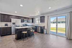 Kitchen featuring dark brown cabinets, stainless steel appliances, a kitchen island, light hardwood / wood-style floors, and a textured ceiling