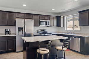 Kitchen with sink, a kitchen island, dark brown cabinetry, light hardwood / wood-style floors, and appliances with stainless steel finishes