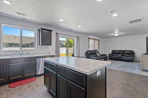 Kitchen with stainless steel dishwasher, sink, a kitchen island, light hardwood / wood-style flooring, and a textured ceiling