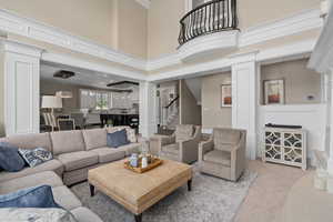 Carpeted living room featuring decorative columns and a towering 25' ceiling. Juliet balcony with iron railing over looking great room.