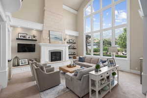 Living room with light colored carpet, a large fireplace, and a towering ceiling