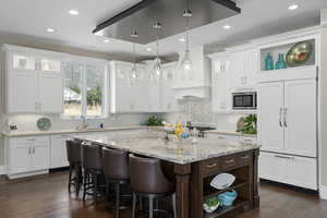 Kitchen featuring built in appliances, custom exhaust hood, hanging light fixtures, and dark wood-type flooring