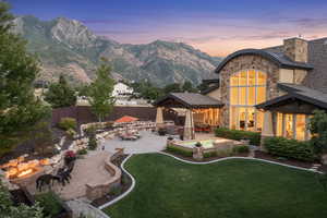 Back house at dusk with a mountain view, a patio, an outdoor fire pit, and a lawn