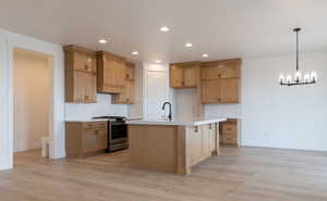 Kitchen featuring backsplash, light hardwood / wood-style floors, gas range, and a center island with sink