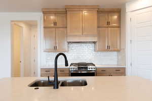 Kitchen with tasteful backsplash, stainless steel gas range oven, sink, light stone countertops, and custom range hood